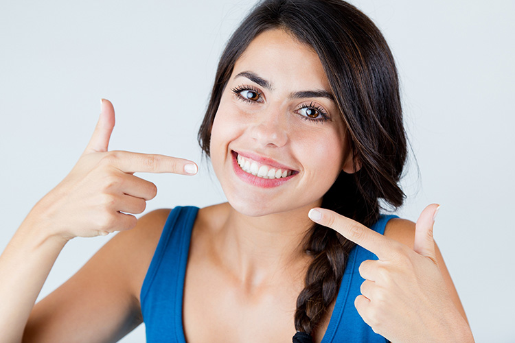 Smiling Female Dental Patient Proudly Points To Her Healthy Teeth